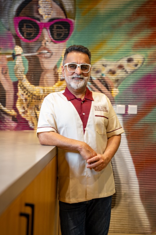 Chef Vineet Bhatia MBE in a Naan & Co shirt, standing in front of the Naancy mural